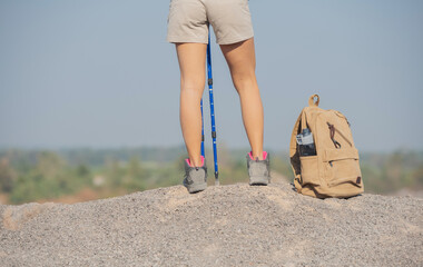 woman hiking in the mountains standing on rocky summit ridge with backpack and pole looking out over landscape. Traveler resting on a mountain plateau. POV view, legs close up on the background.