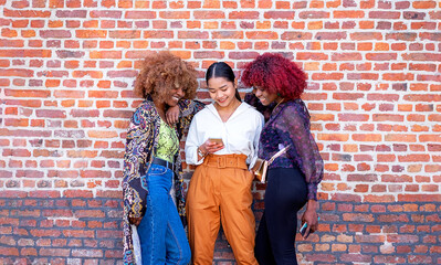 group of female mixed race friends smiling while using a mobile phone. outdoor z generation
