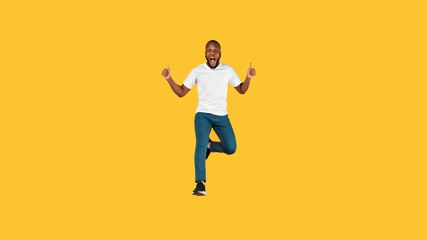 Emotional Black Guy Jumping Gesturing Thumbs Up Over Yellow Background