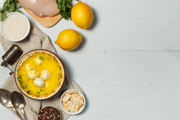 A bowl of avgolemono chicken soup, with meatballs. Flatlay on a gray wooden table. With food for cooking, horizontally, copy space