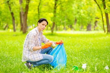 Girl volunteer collects trash in the park in a plastic bag. Ecology care concept