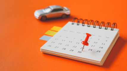 close up of red thumbtack on white page of calendar and blurred miniature silver car for business and finance background , new car, goal concept