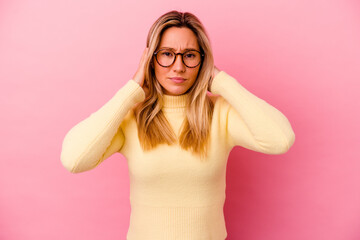 Young mixed race woman isolated on pink background covering ears with fingers, stressed and desperate by a loudly ambient.