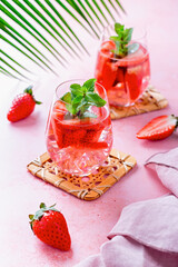 Summer mint and strawberry infused water on pink table top, still life, top view. Summer fruity refreshing cocktail still life closeup
