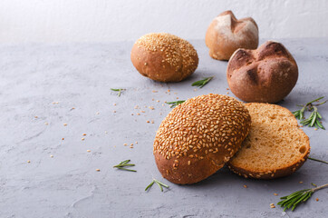 Closeup of rye buns with sesame, fresh herb rosemary on the grey table.Empty space