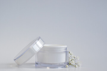Fototapeta na wymiar Layout of an empty jar and flowers for cream, mask, scrub. A jar of cream on a white background. Natural cosmetics and perfumes. Spa treatments. A place for branding and product presentation.