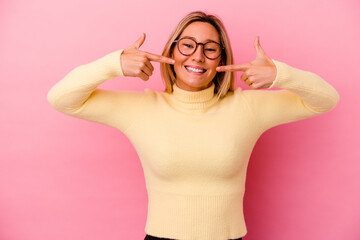 Young mixed race woman isolated on pink background smiles, pointing fingers at mouth.