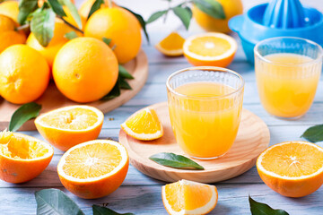 Two glasses of fresh juice, fruit squeezer and ripe fresh oranges on blue wooden table top, fresh orange juice making, top view