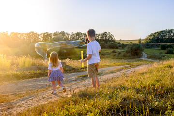 Happy children playing with soap bubbles on a summer nature. Bubbles in the sunset