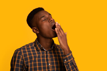 Closeup shot of tired young black man yawning over yellow background