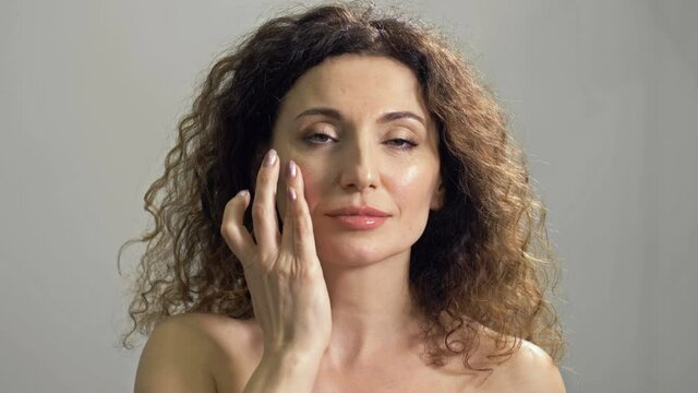 Beautiful mature woman applies cream to the skin of her face with light movements. Body care. Cosmetic and anti-aging treatments.