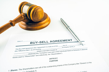 Buy and sell agreement contract closeup with pen, gavel and striking block.