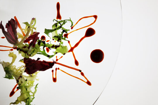Gocce di aceto balsamico tradizionale tipico di Modena in abbinamento con insalata su piatto trasparente. Ripresa dall&rsquo;alto con fondo bianco