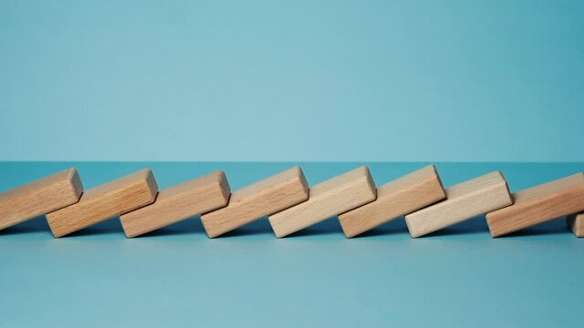 Domino effect, row of wooden domino falling down with light blue background.