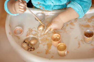 Child's hand paints Easter eggs. Top view. Happy Easter. The child develops fine motor skills with bright paints and quail. 