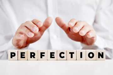 Businessman holding his hands protectively over the wooden cubes with the word perfection. Business service excellence