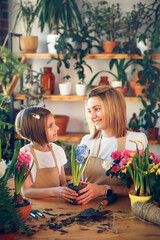 Cute child girl helps her mother to care for plants. Mom and her daughter engaged in gardening. Happy family in spring day.