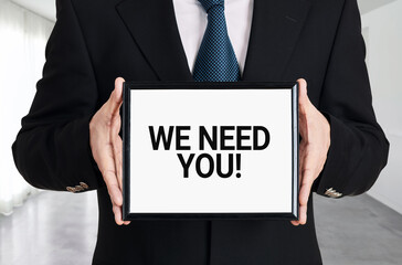 Obraz premium Businessman holds a signboard with the message we need you. Human resources recruitment or employment