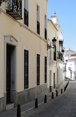 Fototapeta premium Una calle con casas bajas encaladas, con elementos de protección de aceras y farolas negras de metal