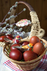 Obraz na płótnie Canvas Toy birds sit in a wicker basket on painted eggs. In the focus of the cake and willow branches. The concept of celebrating Easter