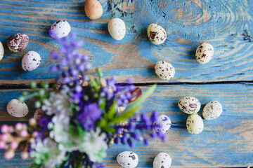 Bouquet of spring purple flowers and a scattering of quail eggs on an old, worn blue table. Vintage...