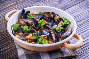 Boiled mussels in cooking dish with parsley on a wooden background