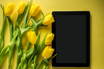Mockup computer tablet with bouquet of tulips on top view on colorful yellow background, panoramic shot