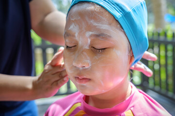 mom applying sunscreen on girl face before swim.