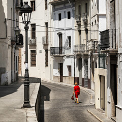 Alte Dame geht im roten Kleid durch eine spanische Stadt.
