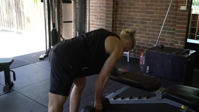 Tattoo man muscles in home gym doing right arm dumbbell lat row bent over