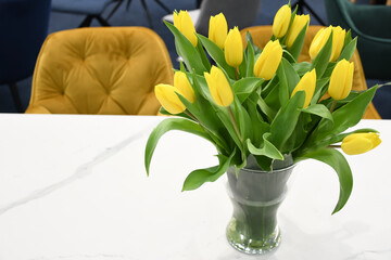 A bouquet of yellow tulips in a glass vase stands on a white table. Home interior