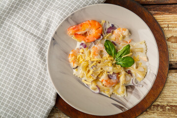 Farfalle pasta with shrimps in a creamy sauce on a gray plate on a wooden table on a light napkin.