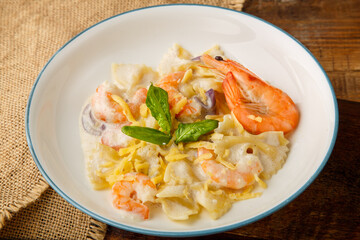 Farfalle pasta with shrimps in a creamy sauce on a gray plate on a wooden table on a linen napkin.