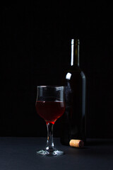 A glass of homemade wine next to a bottle on a dark background. Glass of red wine on a black background. Alcoholic drink