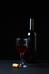 A glass of homemade wine next to a bottle on a dark background. Glass of red wine on a black background. Alcoholic drink