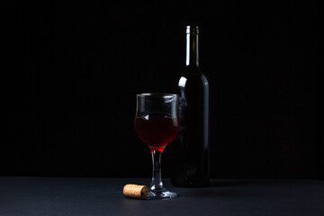 Obraz na płótnie Canvas A glass of homemade wine next to a bottle on a dark background. Glass of red wine on a black background. Alcoholic drink