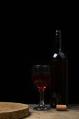 A glass of homemade wine next to a bottle on a dark background. Glass of red wine on a black background. Alcoholic drink