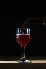 Homemade red wine is poured into a glass on a dark background. Glass of red wine on a black background. Alcoholic beverage