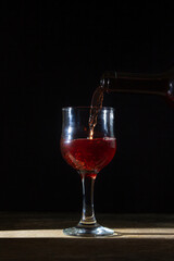 Homemade red wine is poured into a glass on a dark background. Glass of red wine on a black background. Alcoholic beverage