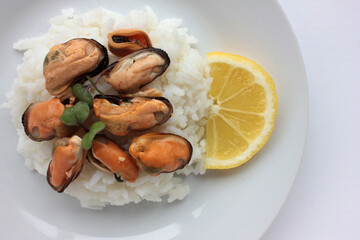 Dish with mussel risotto on white background. Top view of white rice with seafood and lemon slice. Copy space. Healthy eating concept

