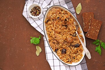 Bigos, fresh and sauerkraut stew with prunes and pork ribs in a white ceramic dish on a brown concrete plate. Cabbage recipes. Comfot food.