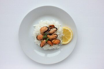 Dish with mussel risotto on white background. Top view of white rice with seafood and lemon slice. Copy space. Healthy eating concept
