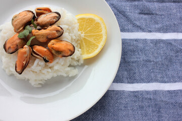 Mussel risotto on white plate on table. Top view of white rice with seafood and lemon slice on striped cloth napkin background. Copy space. Healthy eating concept
