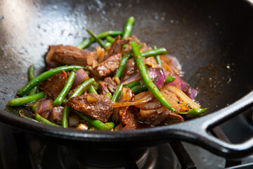 Tri-tip steak, green beans strings, onions in a cast iron cooking wok. Sautéed in organic oysters sauce.