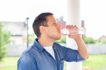 Close up of a man drinking water from bottle outdoor. Man refreshing himself. Thirsty man drinking water from a plastic bottle in summer park. Healthcare concept. Young Man drinking water after sport
