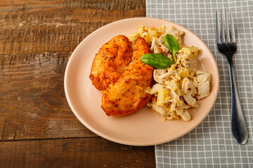 Baked chicken breast on a beige plate with pineapple salad on a table on a round stand
