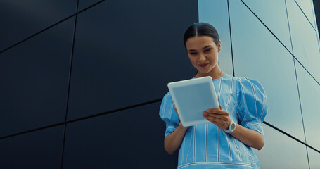 low angle view of happy woman in blouse using digital tablet near building