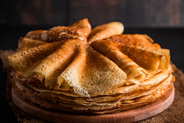 A stack of thin pancakes on a dark wooden background. A traditional dish of crepes for the holiday Maslenitsa.