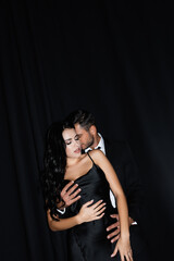 Young man hugging sexy woman in satin dress on black background