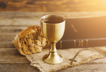 Chalice of wine with bread and Holy Bible on wooden background